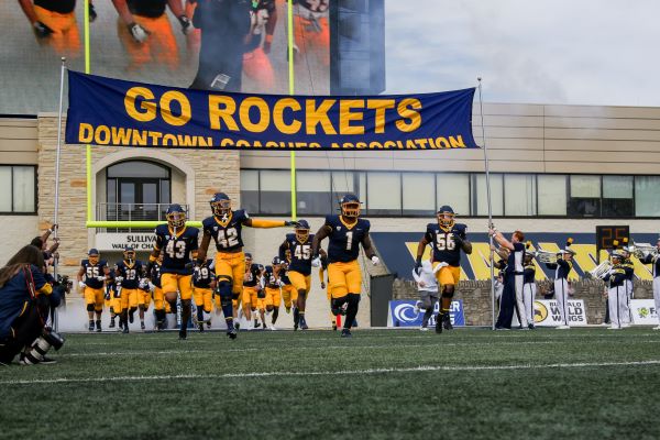The football team running onto the field with a "Go Rockets" banner