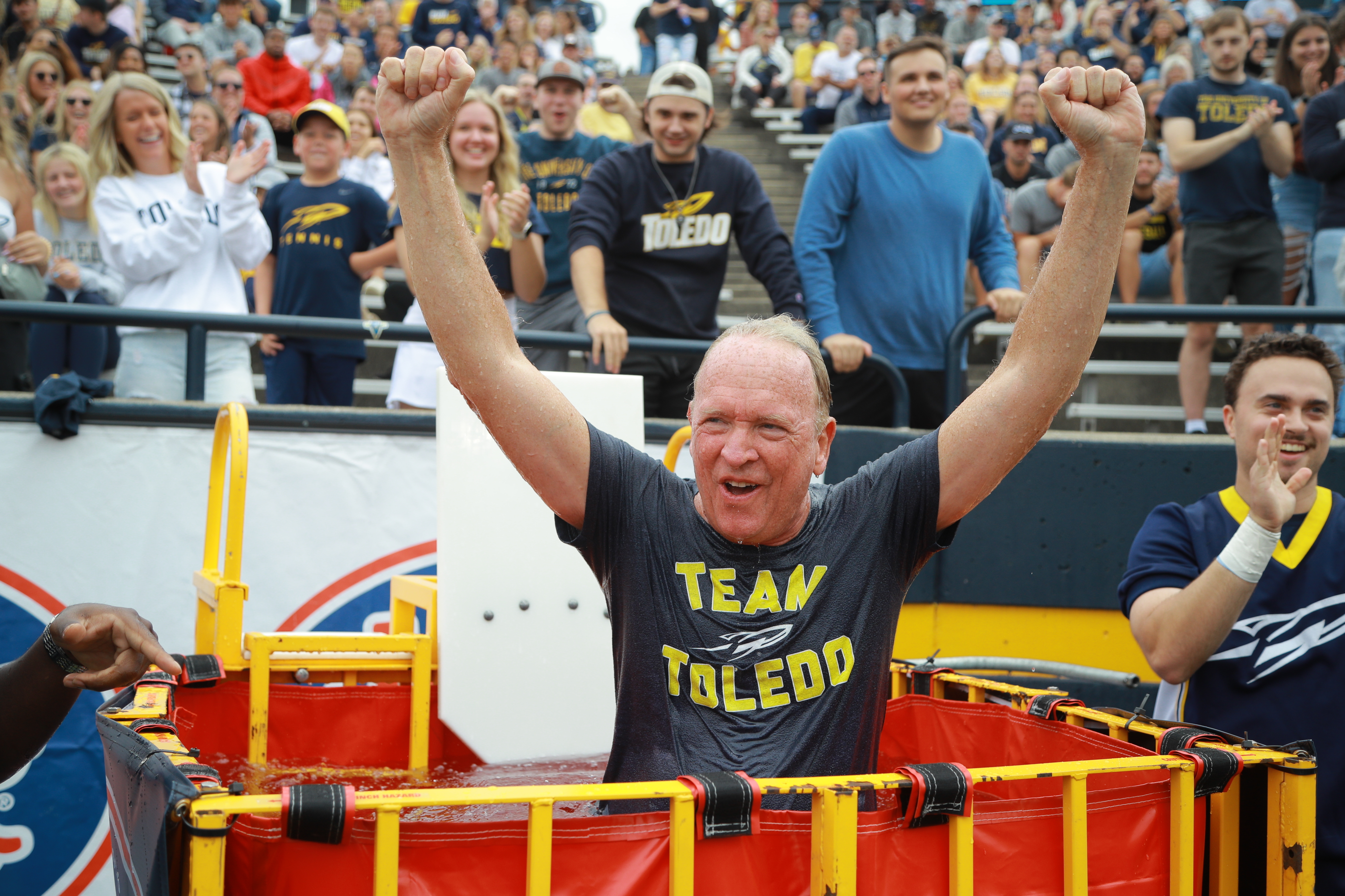 A photo of University of Toledo President, Dr. Gregory Postal, posing with his hands in the air after being dunked in the Touchdown Tank, a dunk tank used after Toledo scores a Touchdown during games.